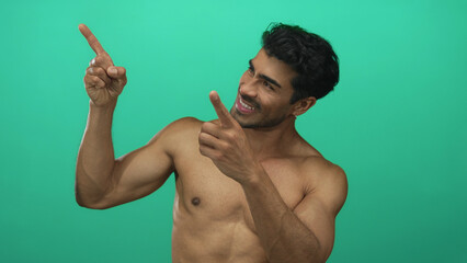 Man pointing fingers upward with bare chest in bright green studio for dynamic energetic gesture; confidence.