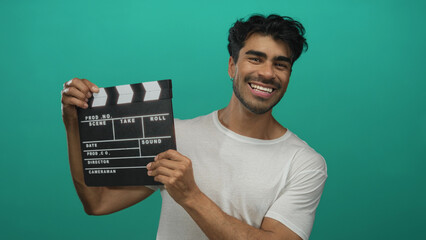 Hispanic man in white t shirt holding film clapboard against vibrant green studio wall with...