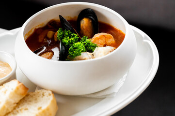 A rich, vibrant bowl of seafood stew with mussels, shrimp, and crab meat, garnished with fresh parsley and served with toasted bread and aioli on a white plate