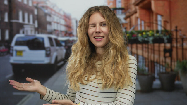 Confident woman with hand raised presenting street scene captures a blonde young model smiling against an urban outdoor city backdrop.