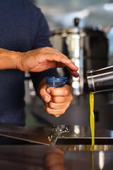 Farmer hands hold blue tasting cup of EVO oil. Blurred industrial mill background. Natural light. Professional expert tasting.