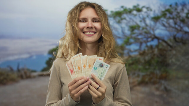 Woman holding banknote smiling in outdoor scene highlights blonde young money cash finance fan energy.