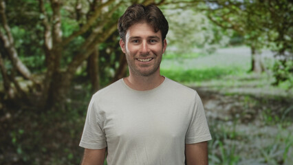 Man smiling with face visible and relaxed posture in a green park forest setting; serenity friendly.
