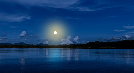 A moonlit lake with mountain shadows and soft clouds reflects the tranquility of the night.