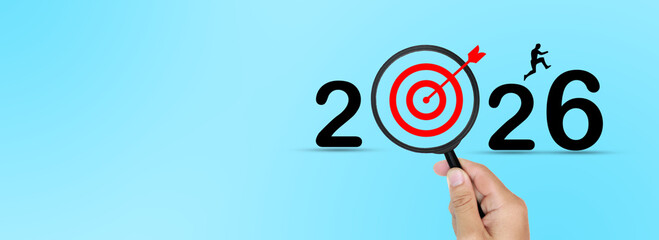 The 2026 goal is a hand holding a magnifying glass highlighted in red, representing vision,...