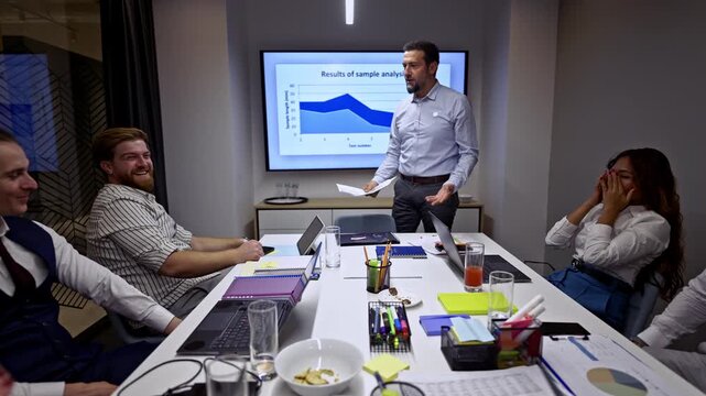 A group of business people engages in a crucial corporate meeting, where a male presenter discusses sample analysis results. The team collaborates, exchanging ideas and planning future strategies.