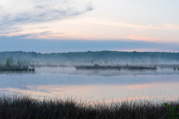 In the early morning a lake with a reflection of the sky. The sky is overcast and the air is cool and damp. The scene is quiet and peaceful, with the lake providing a sense of solitude and calm. Dwing