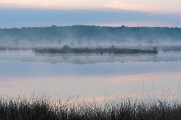 In the early morning a lake with a reflection of the sky. The sky is overcast and the air is cool and damp. The scene is quiet and peaceful, with the lake providing a sense of solitude and calm. Dwing