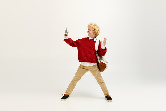 Child in stylish outfit posing joyfully with a smartphone in a bright studio setting
