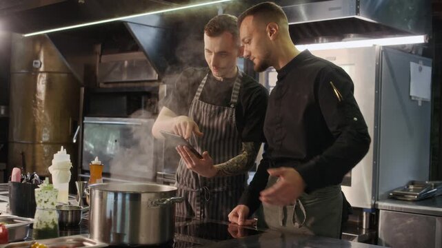 Medium shot of two professional chefs cooking together in restaurant kitchen and using digital tablet, scene lit by cinematic lighting, copy space