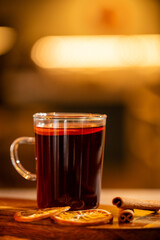 A glass of mulled wine with orange slices and cinnamon sticks on a wooden table in warm lighting