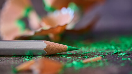 Green pencil near shavings on wooden table