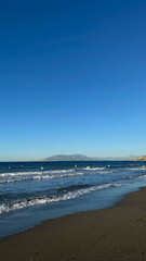 Serene beach landscape with gentle waves lapping at the shore under a clear blue sky, creating a peaceful coastal atmosphere for relaxation