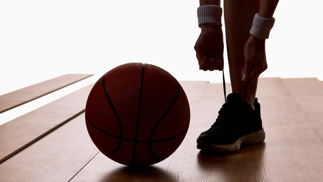 Basketball ball on floor next to athlete tying shoelaces before training. Concept of preparation, discipline, sports motivation, and focus for digital and editorial visuals. - Powered by Adobe