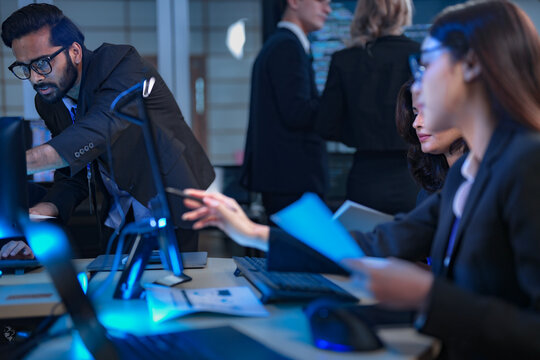 A team of financial analysts works through the night in a fast-paced firm, processing market data, reviewing performance reports, and executing trades to manage investment portfolios.