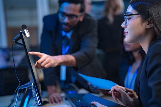 A senior data scientist with glasses points out an anomaly in a machine learning model's code to two female AI engineers, as they finalize the algorithm for a new predictive analytics service.