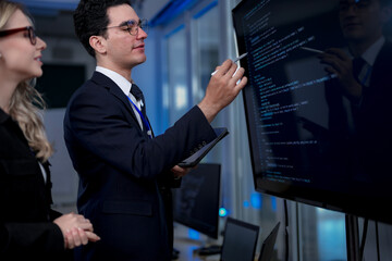 Fototapeta premium A male team leader in a suit uses a stylus to explain a complex project on a large screen, providing one-on-one training to a female colleague in a modern, high-tech office.