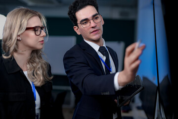 A senior software developer leads a code review session, pointing to a specific function on the screen to explain its logic and syntax to a junior engineer before a major deployment.