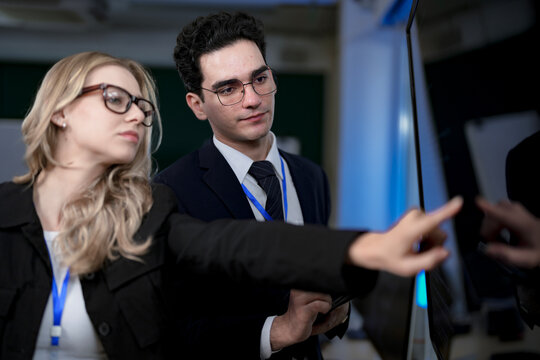 A senior software developer leads a code review session, pointing to a specific function on the screen to explain its logic and syntax to a junior engineer before a major deployment.