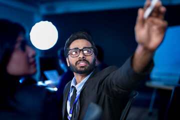 A diverse team of professionals collaborates on a business strategy late at night. A male manager uses a tablet and stylus to explain key points to his female colleague in a modern boardroom.