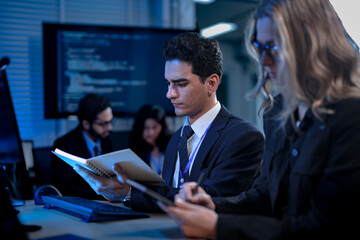 A young male professional in a suit smiles as he points out a successful result on a computer screen to his female colleague, celebrating a project milestone in a modern tech office.