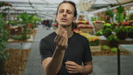 Man pinches fingers by a flower stall on street, long hair tied back, visible hands and open palms,...