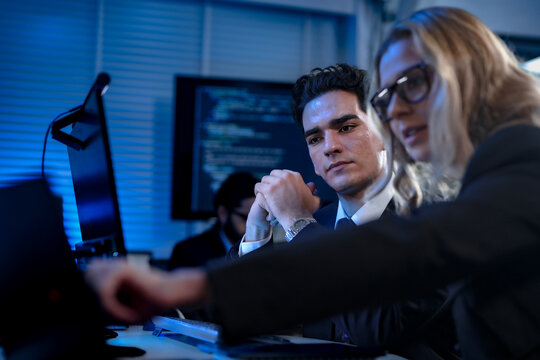 in a coding bootcamp, aspiring software developers take notes during a late-night lecture, studying algorithms and syntax from code displayed on a large screen behind them.