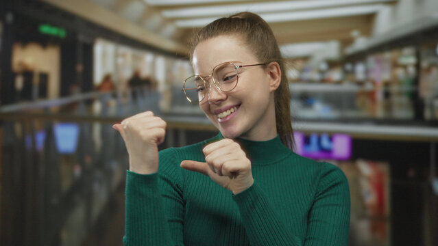 Woman wearing glasses and a green sweater shows face with pursed lips and rests hands on hips in mall; confidence assertiveness empowerment determination.