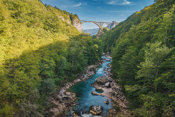 Iconic arched bridge crossing a deep Tara river canyon surrounded by lush green forest and mountains under a blue sky, representing travel and nature