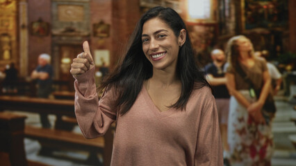 Woman smiling and giving a thumbs up with visible thumb and hand inside ornate catholic church...