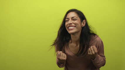 Woman with clenched fists smiling and shouting in a studio set with a lime green wall; pure excitement.