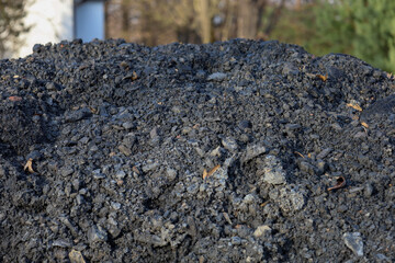 This is a detailed close-up of a large pile of dark, granular material, likely coal or rubble, with an uneven, rough texture. Black and gray fragments of various sizes create a textured background.