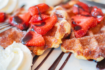 Appetizing Viennese waffles with sliced ​​strawberries and cream, soft focus on background