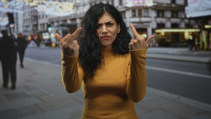 Fototapeta premium Young woman shows middle finger with both hands on busy city street; defiance rebellion attitude boldness.