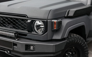 Close-up quarter view of customized off-road truck. Rugged dark gray SUV with textured coating, snorkel, off-road tires, heavy-duty bumper and LED light bar.