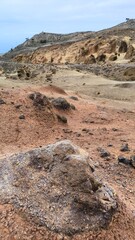 Layered volcanic rocks and eroded slopes form an arid canyon landscape in Upper Teno, Tenerife. Exposed soil layers and unique geology highlight the harsh mountain terrain under a blue sky.