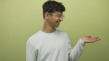 Young hispanic man wearing glasses and white sweater smiling holds open palm in green studio  optimism. © Krakenimages.com