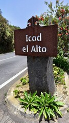 Roadside sign for Icod el Alto mounted on volcanic stone with lush plants and bottlebrush shrub, photographed near Mirador El Lance above Los Realejos, Tenerife, Canary Islands, Spain.