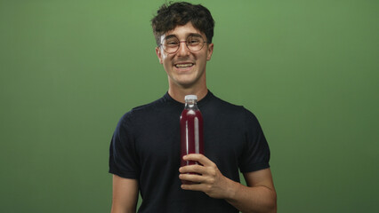 Man holding a clear bottle of purple juice and shrugging while wearing glasses in a green studio; taste uncertainty.