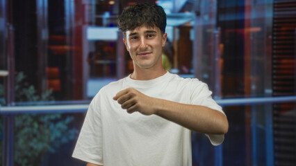 Fototapeta premium Man pointing finger at camera in building lobby wearing white t shirt and relaxed expression; confidence invitation.