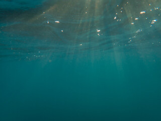 Fototapeta premium Ocean underwater rays of light background, under blue water sunlight. Underwater background, ocean or sea surface seen from under water. Rays of light beams, abstract marine backdrop. Nature landscape