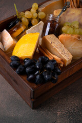 Assorted cheeses, fig jam, honey, grape in a wooden box on a dark background. Gift set idea