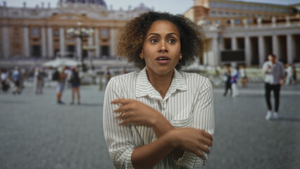 Woman holds arms across chest, hands clasped to collarbone while standing in vatican building...