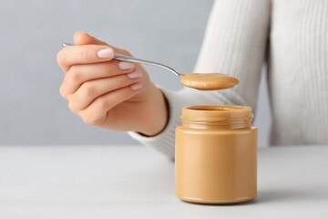 Female hand holding spoon with creamy peanut butter above jar, showcasing delicious texture and inviting presentation, perfect for culinary inspiration and food photography