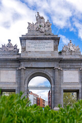 Obraz premium The Puerta de Toledo, a grand stone triumphal arch in Madrid, features three arches and sculptural groups at the center of a traffic circle under partly cloudy skies