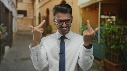 Business casual man in white shirt flips both middle fingers at camera on old town street; bold...