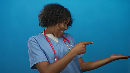 Doctor woman drapes red stethoscope over shoulders and points finger with open palm in blue studio; compassionate care.