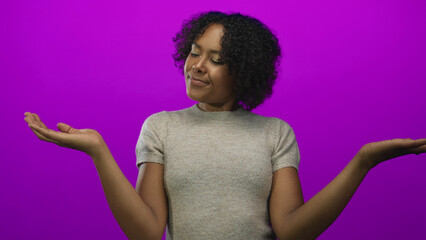Woman in gray sweater outstretches palms and glances at hand in studio under purple light; balance...