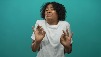 Young african american woman wearing white t shirt cringing while holding ok sign in a teal studio; disgust.