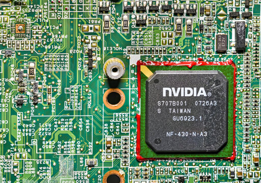 Close-up of a computer circuit board showing a central processing NVIDIA chip surrounded by detailed electronic components, solder points, and green PCB pathways in high-resolution macro view.